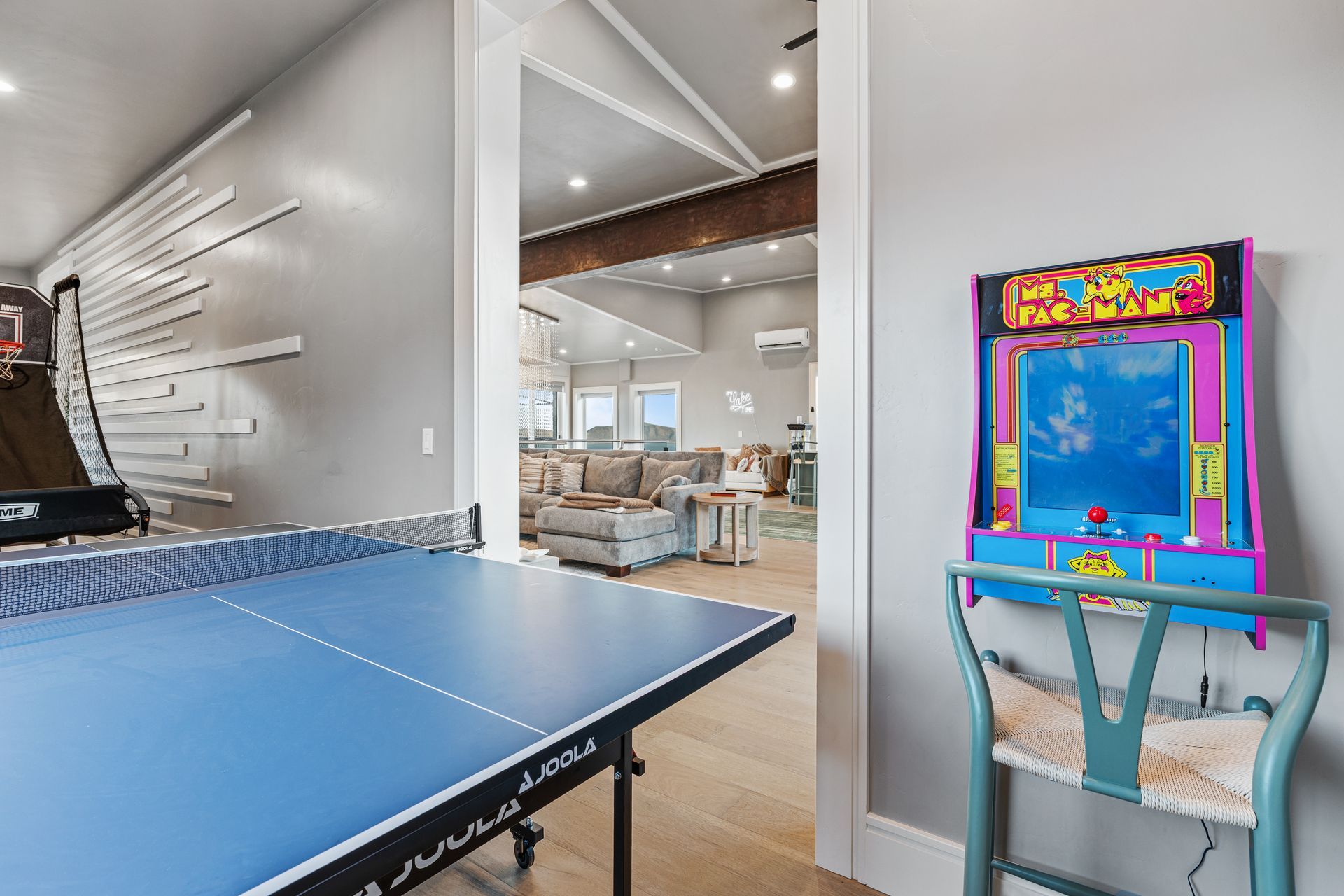 Modern game room with ping-pong table and colorful arcade machine beside a bright living area