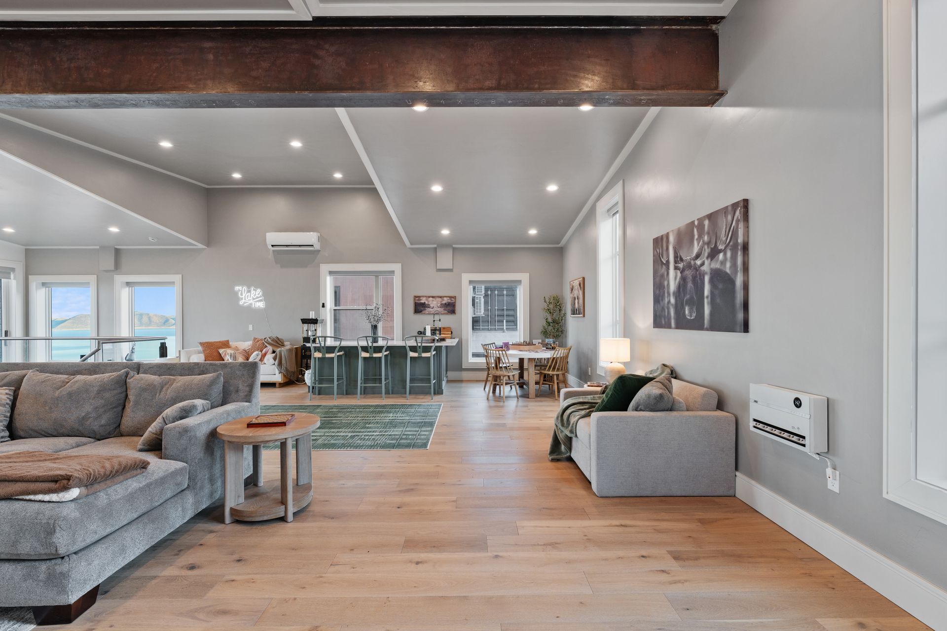Spacious modern living room with gray sectional, wood floors, recessed lights, and open dining area