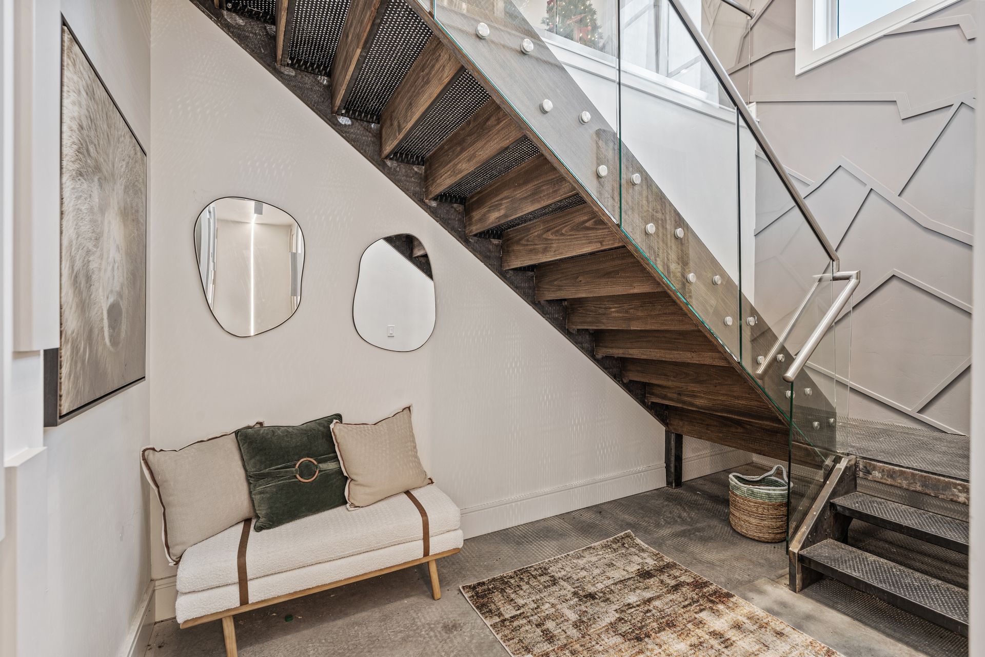 Modern entryway with a staircase, white bench, wall mirrors, and a neutral rug