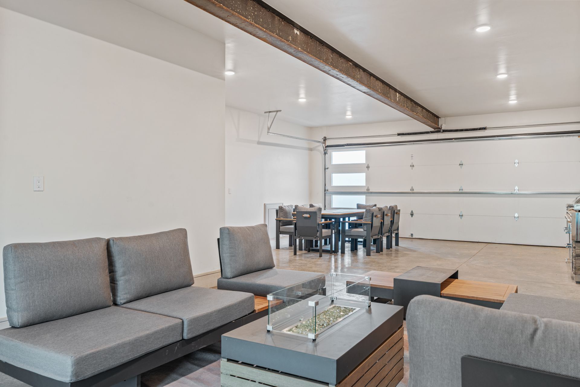 Modern open-concept living room with gray sectional, glass coffee table, dining table, and white walls