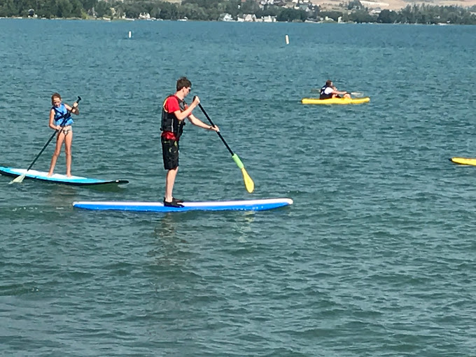 People paddleboarding on a lake, with two standing on blue boards and one on a yellow board in the distance.