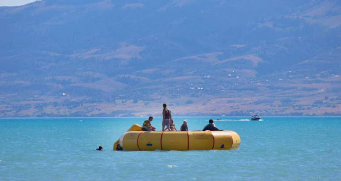 People on a yellow inflatable raft on a blue lake with mountains in the background