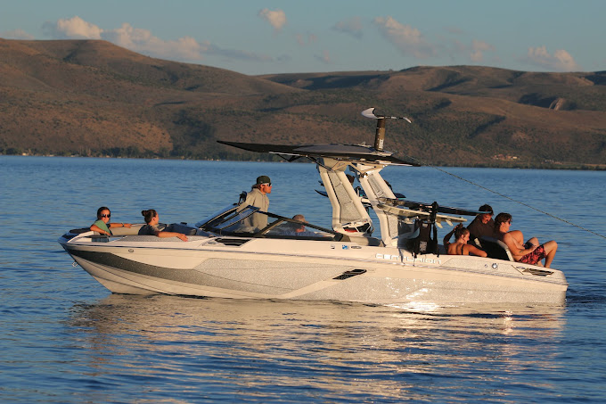 White speedboat with several people on calm blue water near rocky hills at sunset