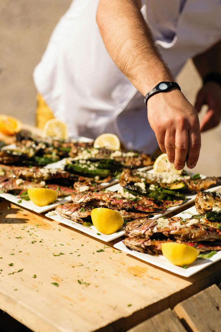 A chef garnishes grilled fish plates with lemon wedges on a wooden table.