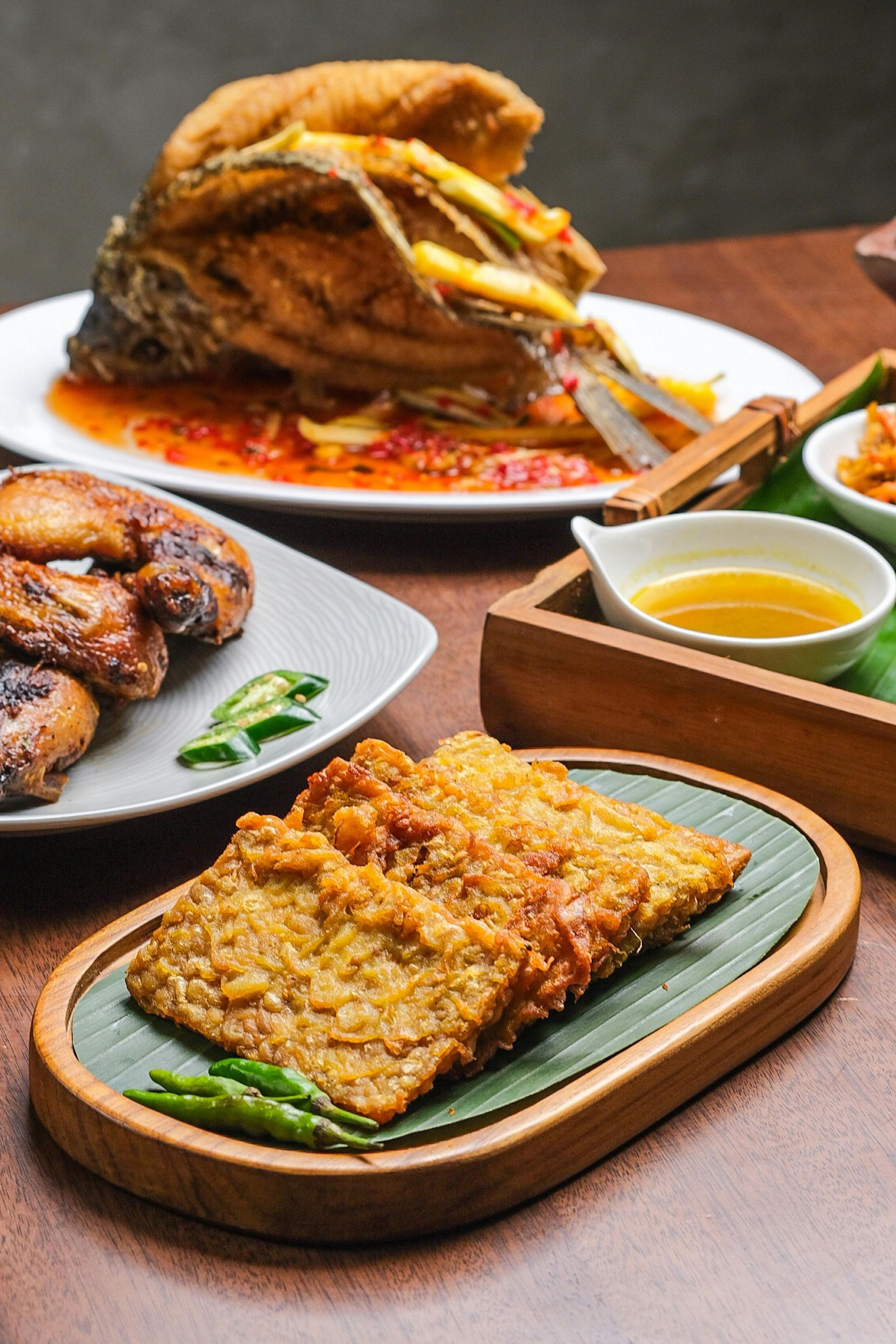 Plated roasted meat and fried dish with dipping sauce on a wooden table, close-up food spread