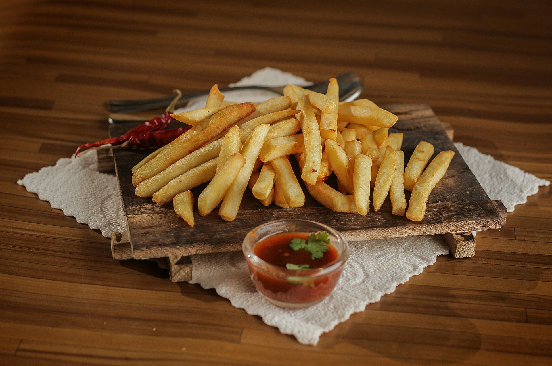 French fries on a wooden board with a small bowl of dipping sauce on a wooden table.