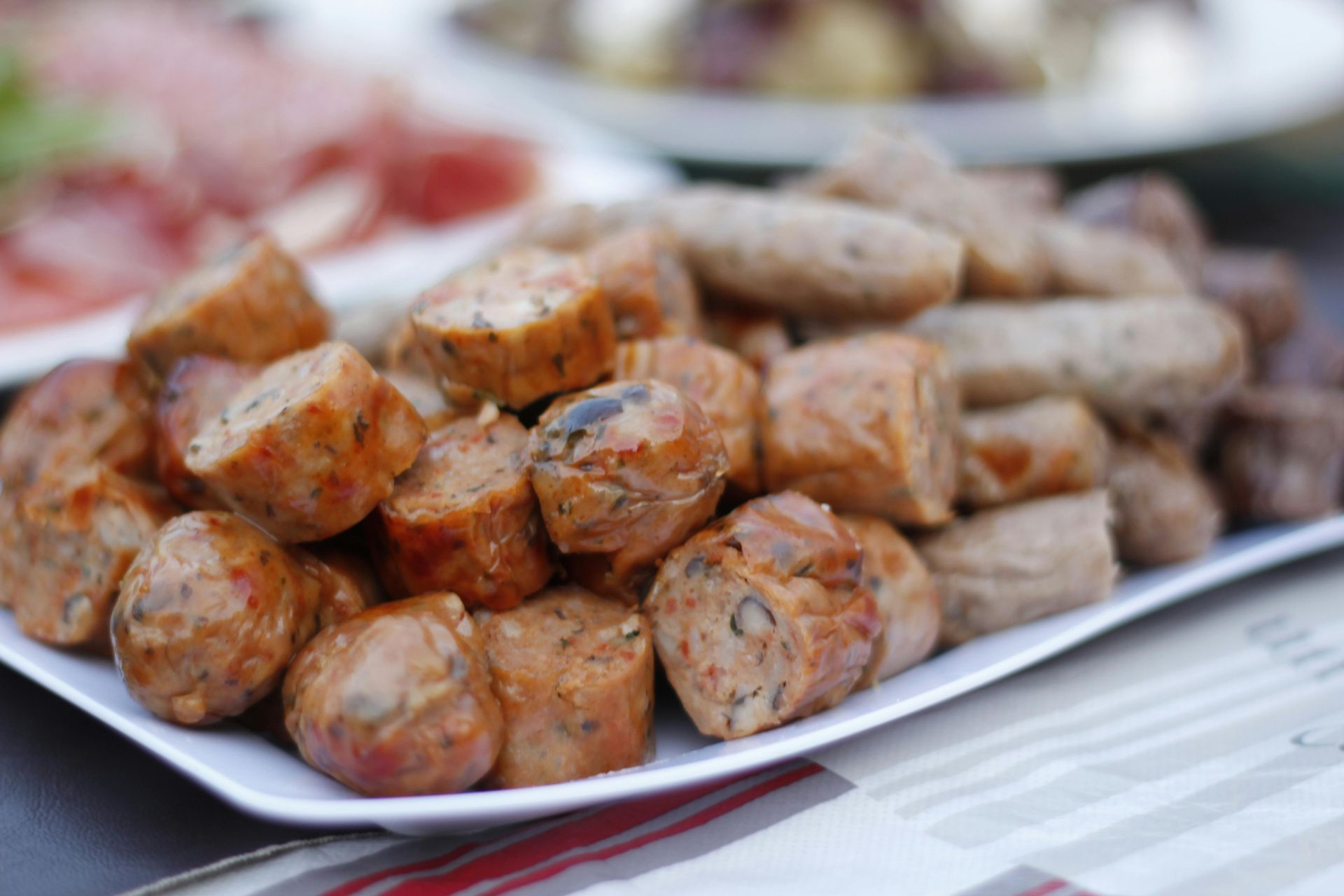 A wooden platter featuring folded slices of chorizo and thin pieces of roast beef, garnished with fresh herbs.