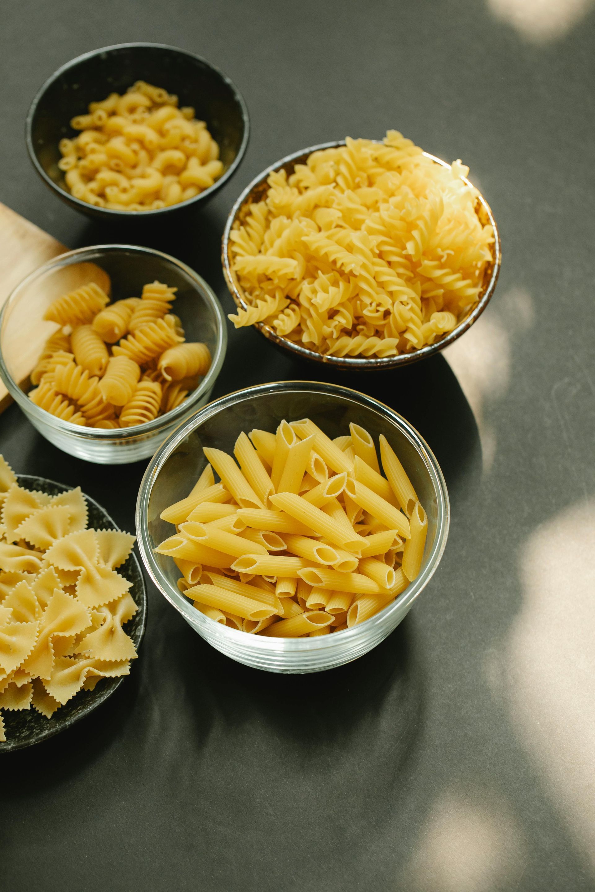 Fettuccine pasta nests, raw eggs, a rolling pin, and small spoons of salt and peppercorns on a rustic wooden table.