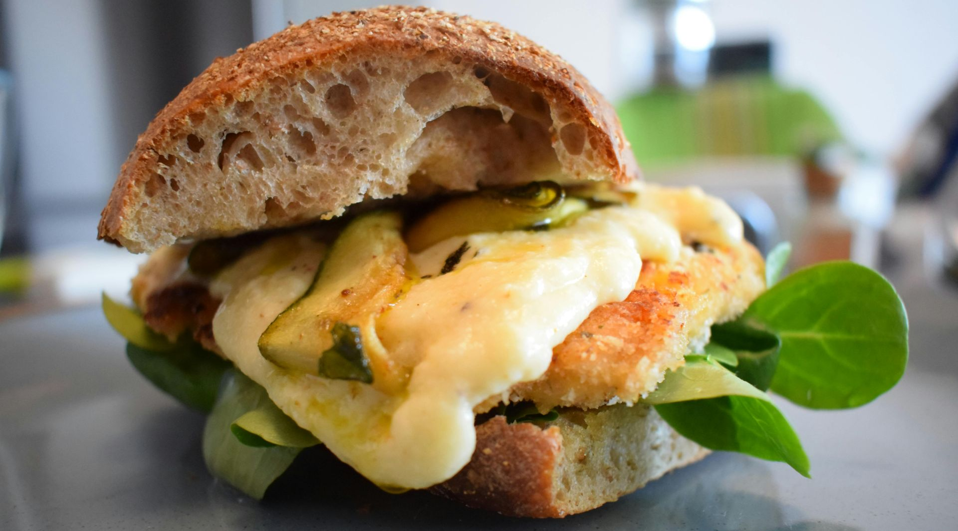 Close-up of a sandwich with melted cheese, greens, and avocado on a table