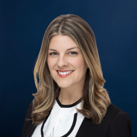 Studio headshot of a smiling woman in a black blazer and white blouse against a blue background