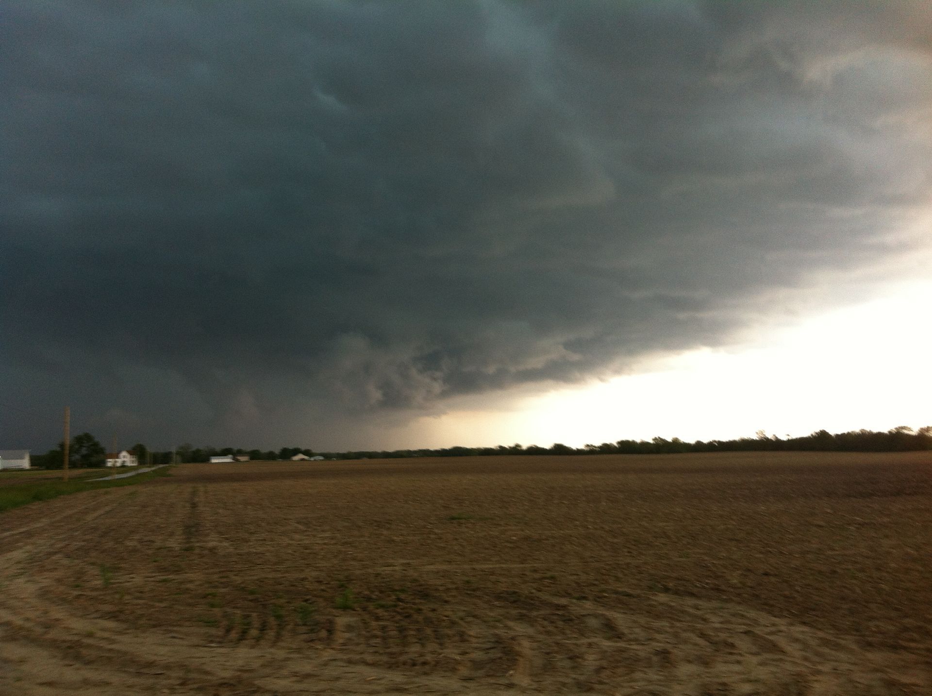 Dark storm clouds over a plowed field with a bright break on the horizon