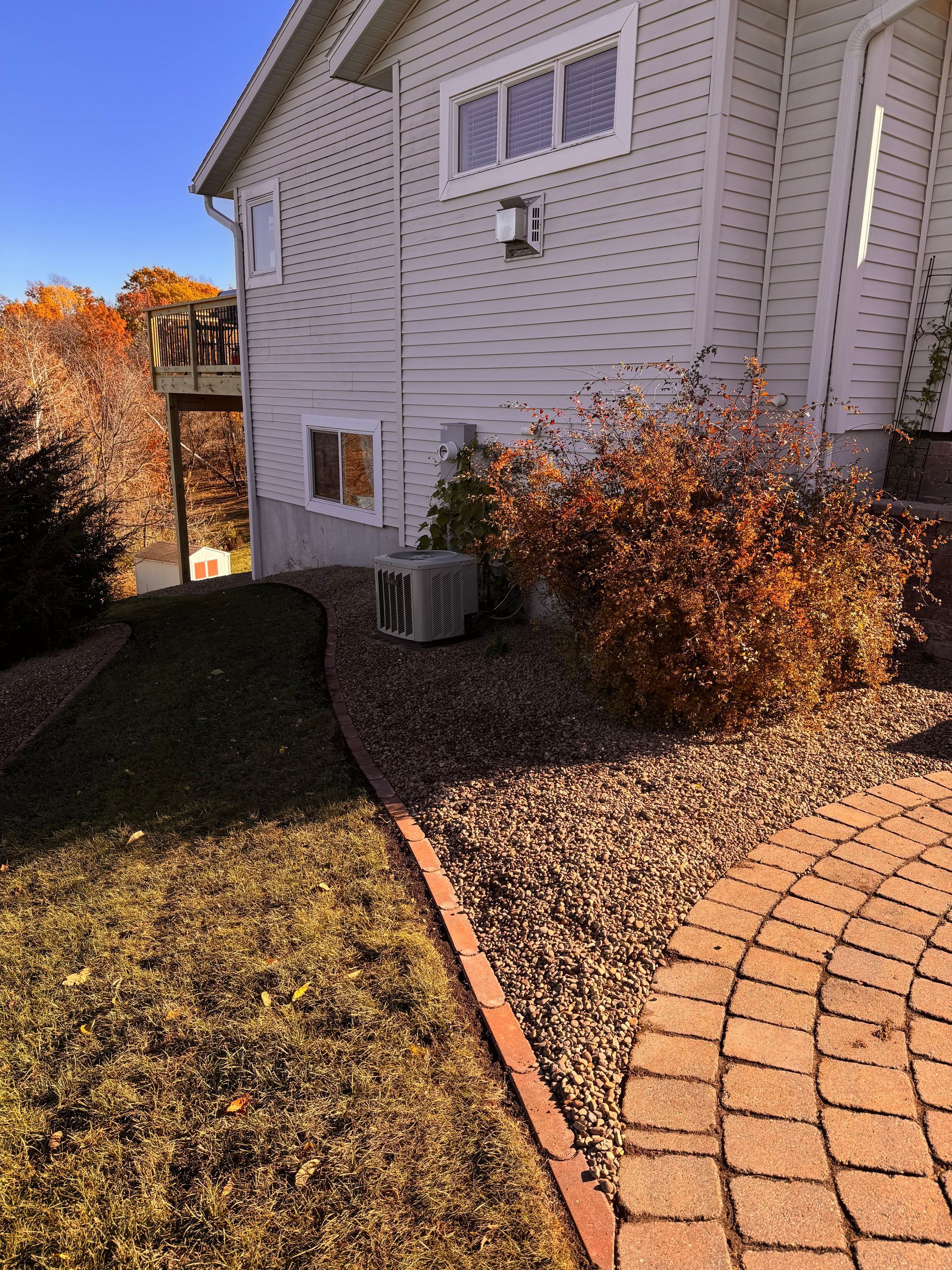 House exterior with tan siding and brick pathway, with fall foliage in a landscaped yard.