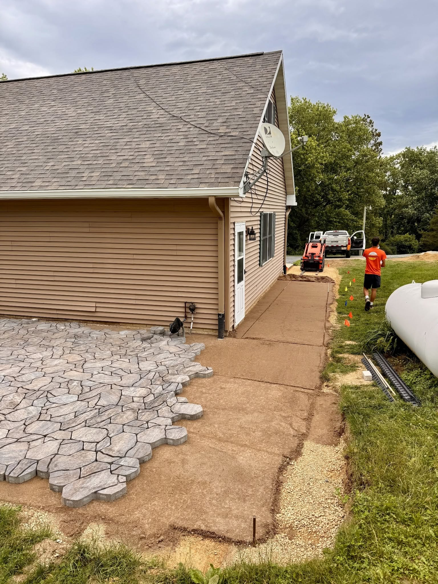House exterior with damaged siding and roof, workers on a side walkway, and gravel piled near the wall