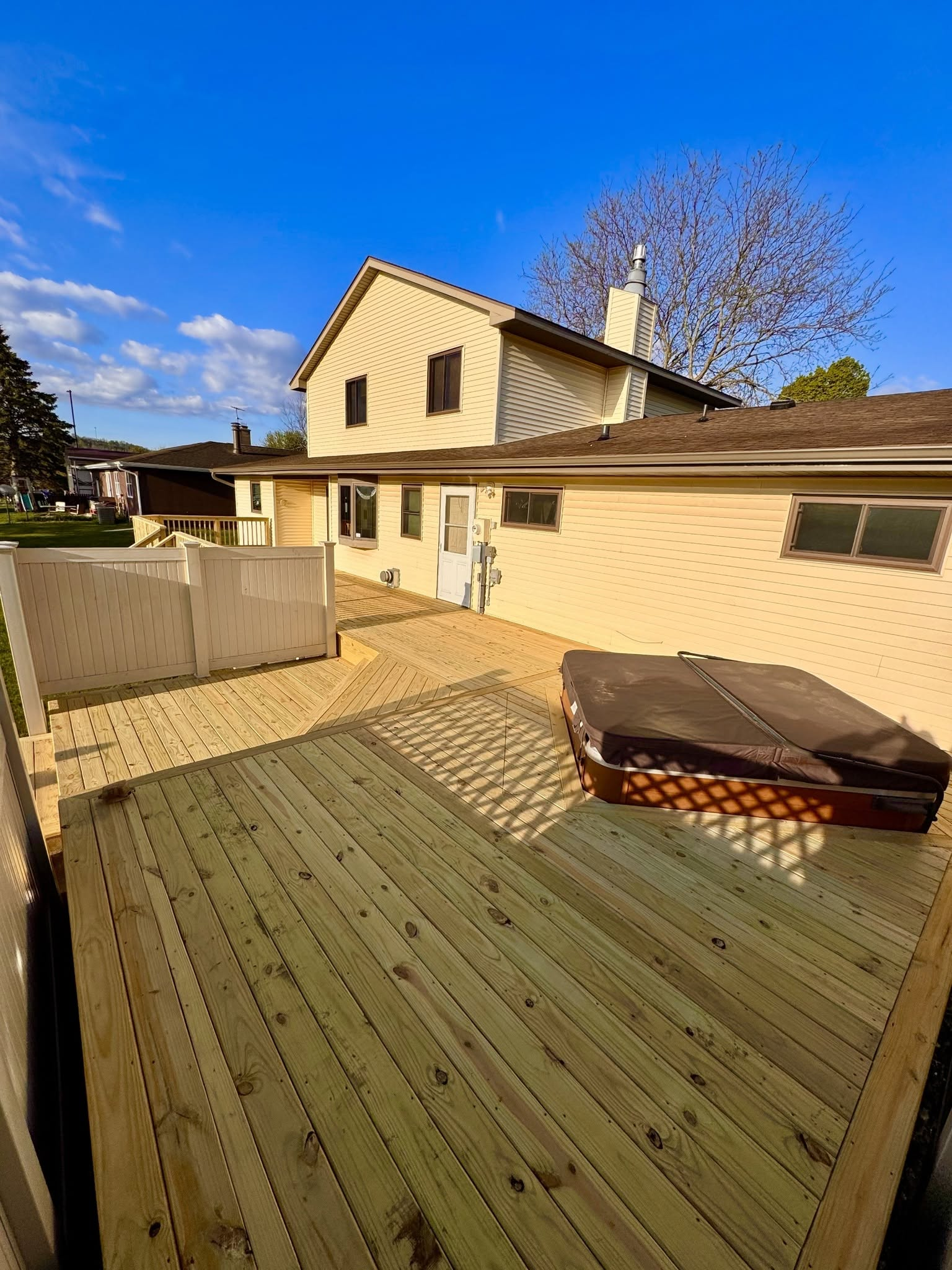 Backyard deck with a hot tub beside a beige house under a clear blue sky