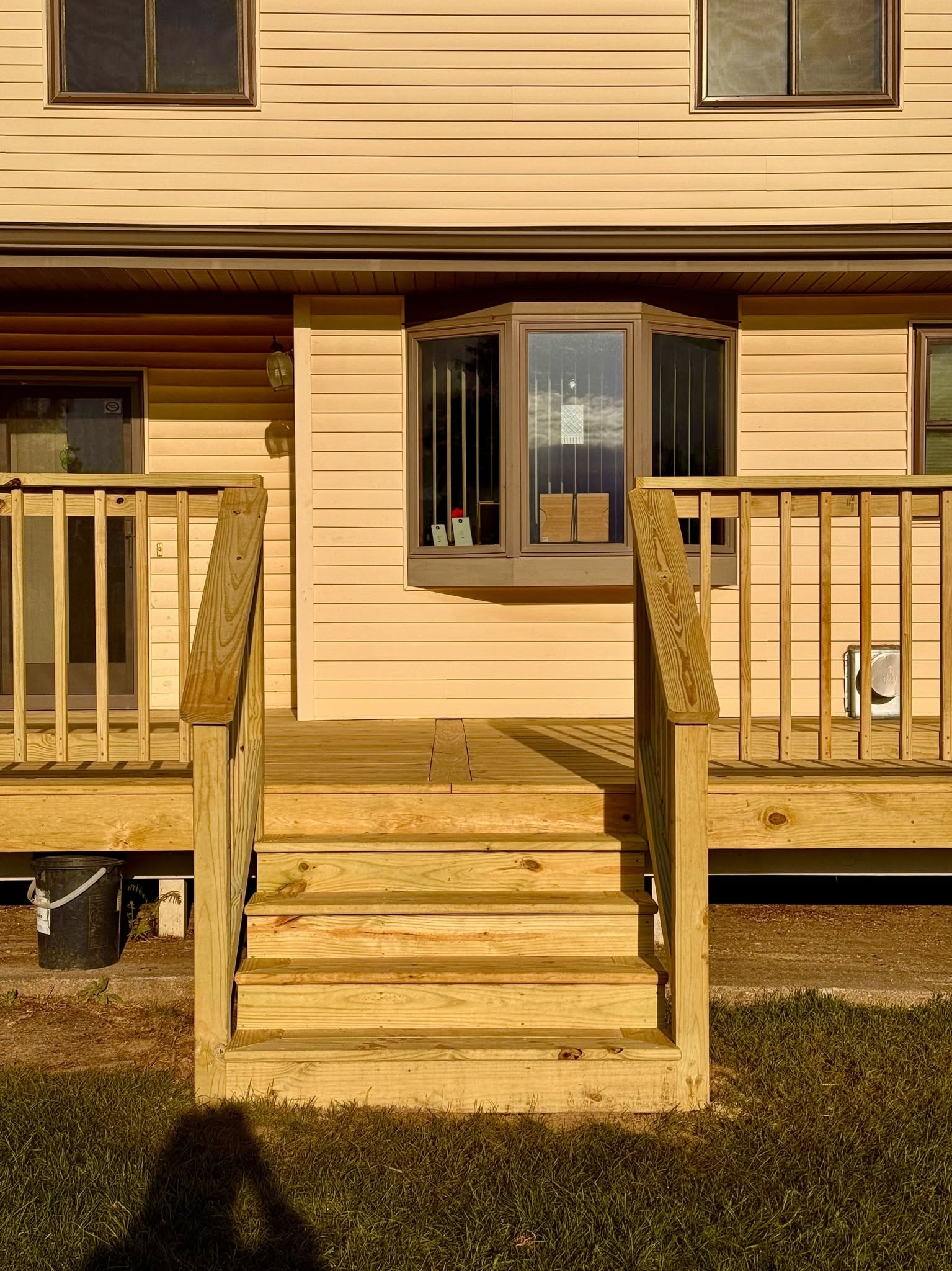 Front porch of a beige house with wooden steps, railing, and a central window.
