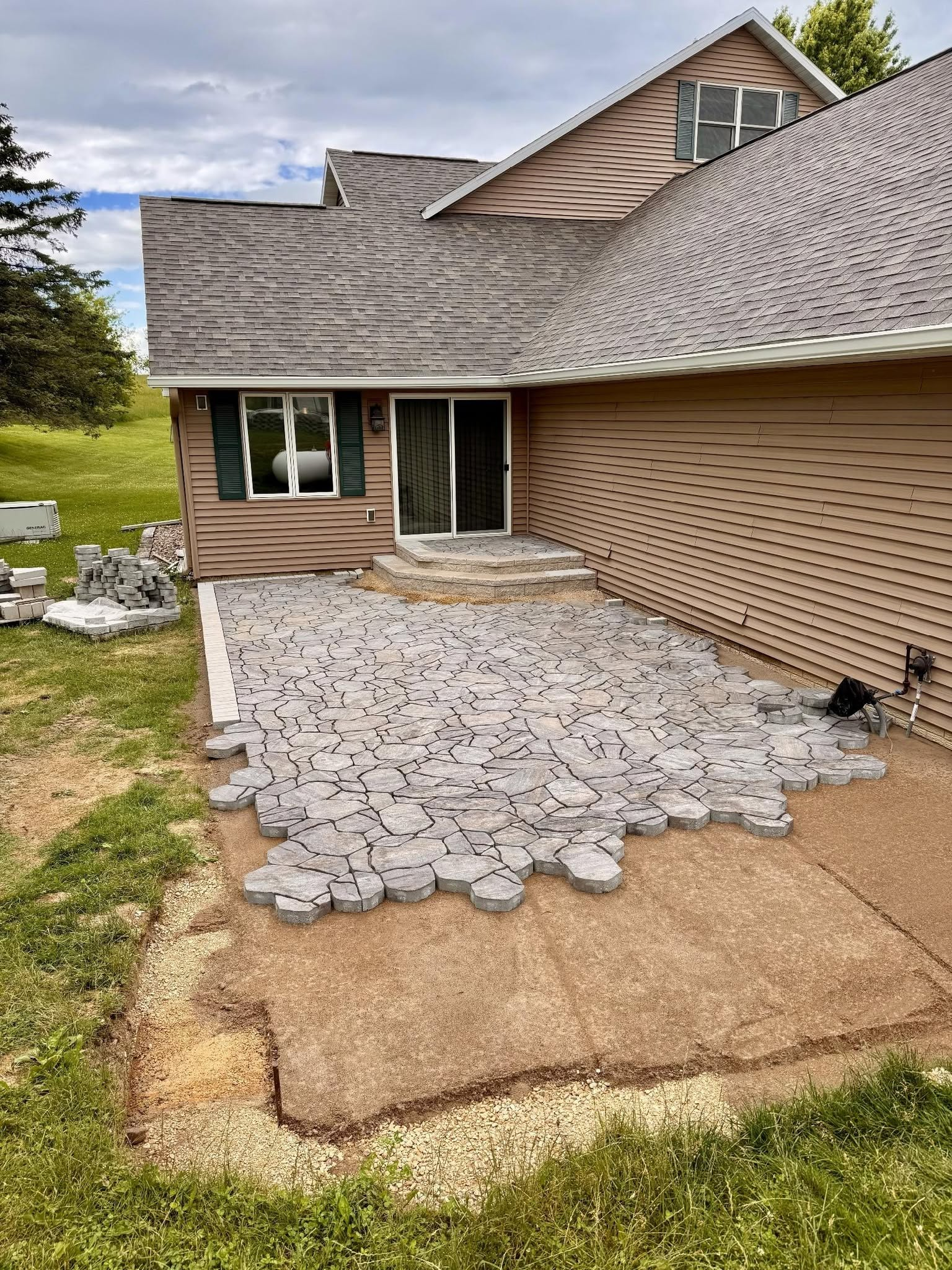 Damaged patio and exterior wall of a house with torn siding and debris, under a cloudy sky