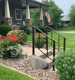 A house with a porch, stairs, flowers and a flag.