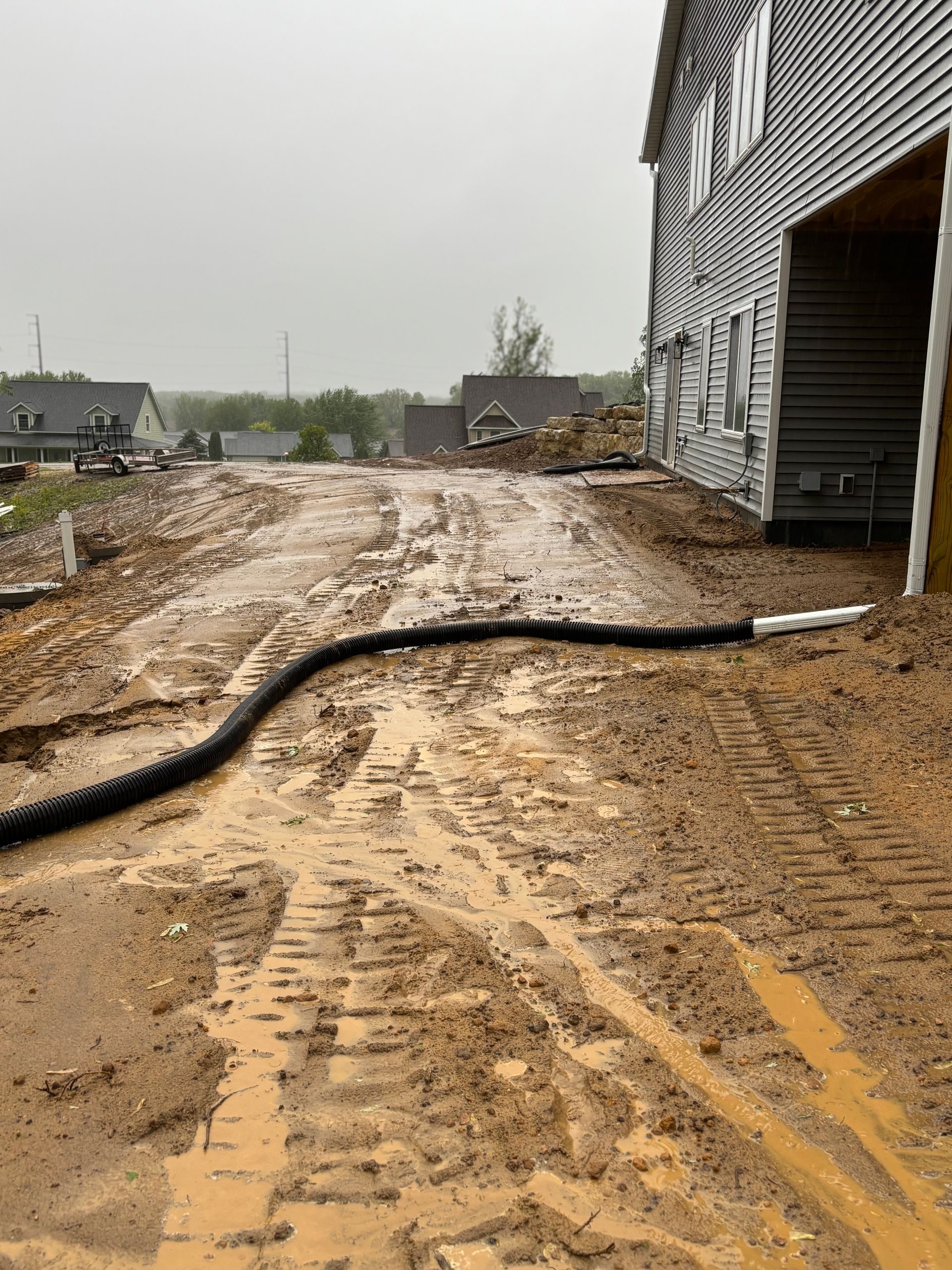 Muddy construction site with a black drainage pipe. A building is on the right.