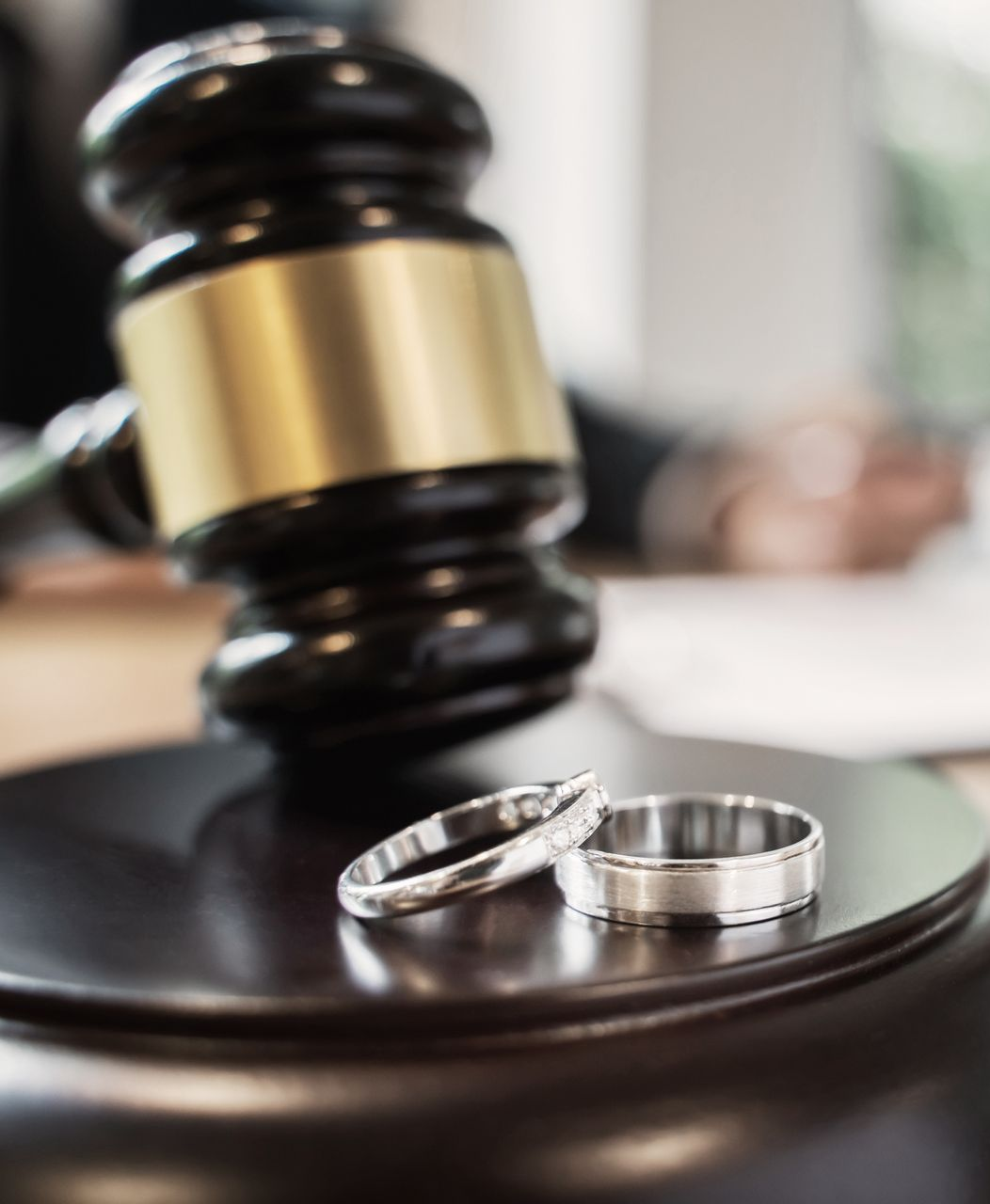 Wedding rings sit below a gavel on a dark wooden block, likely in a courtroom.