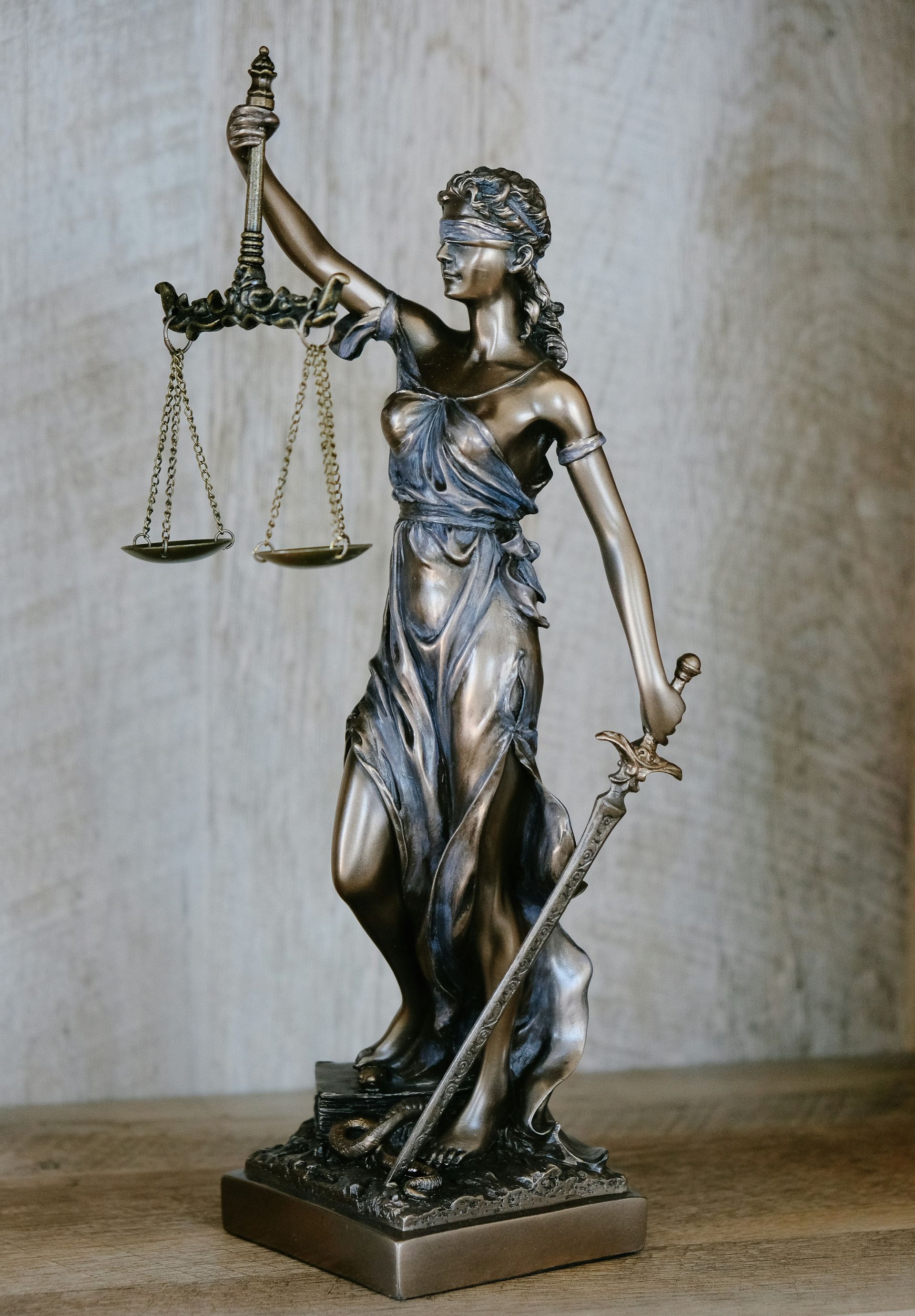 Statue of Lady Justice holding scales and a sword, blindfolded. Bronze with a beige background.