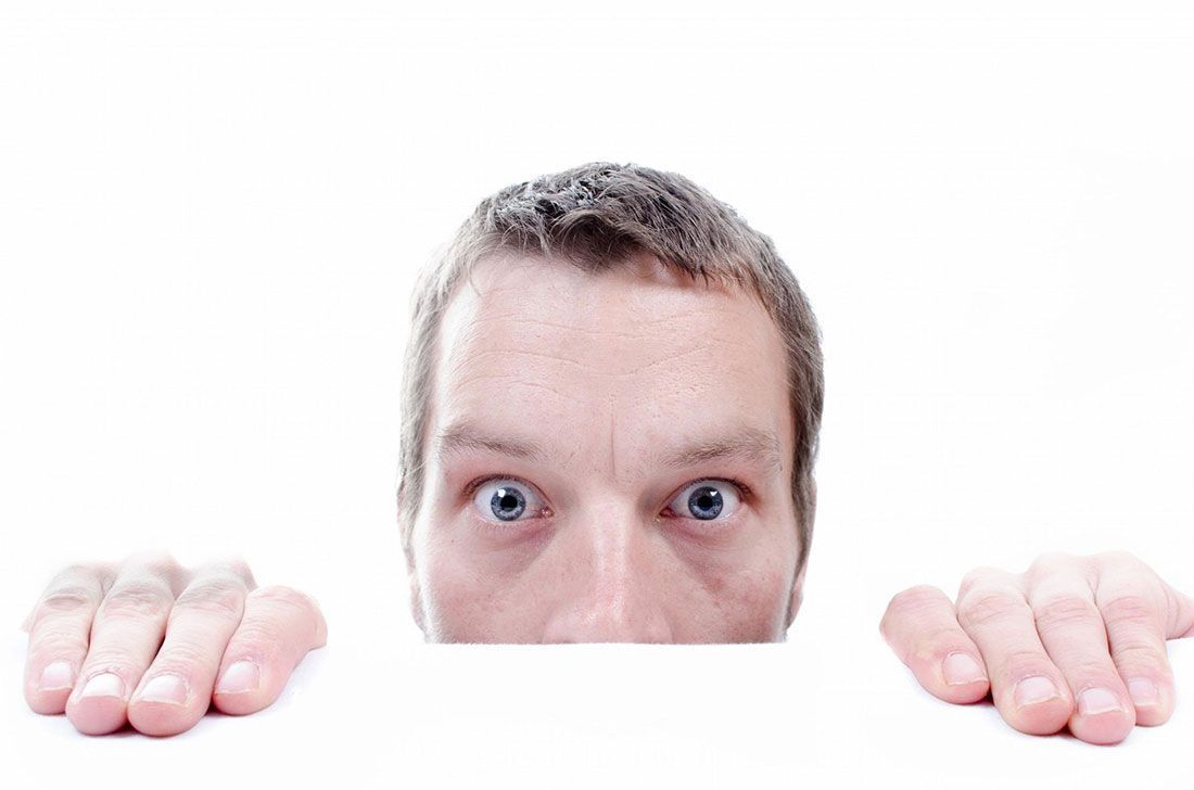 A man is peeking over a sign with his hands