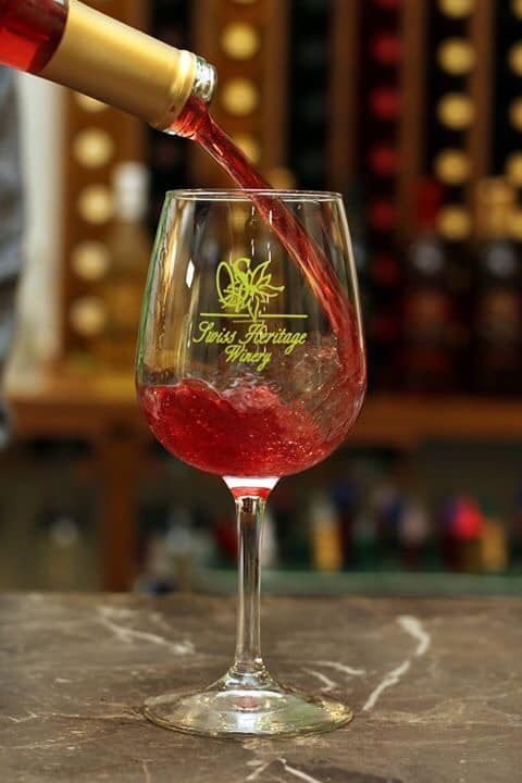 Red wine being poured into a tall wine glass with winery logo.