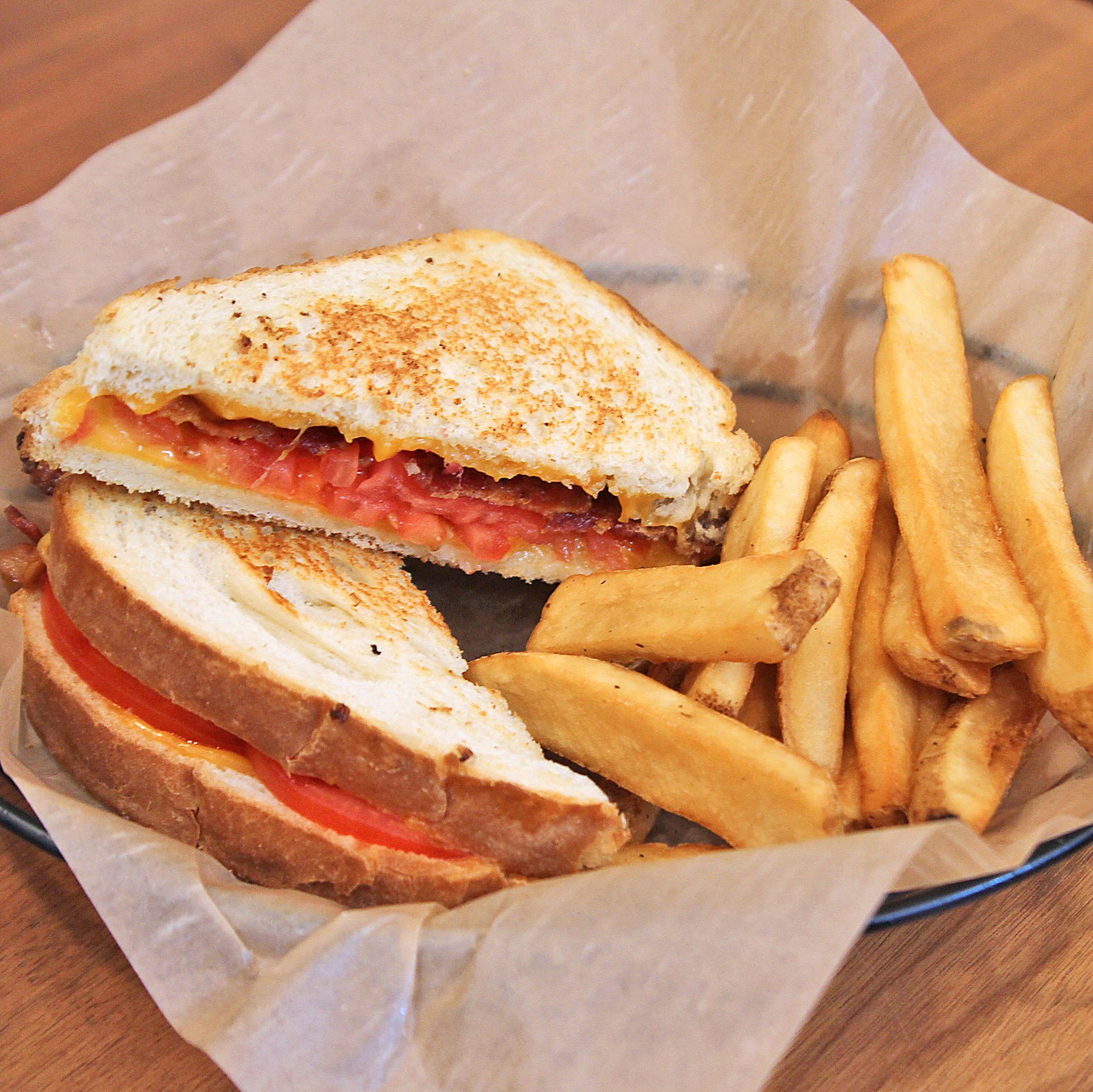 Grilled sandwich with tomato and bacon, served with a side of fries in a basket.