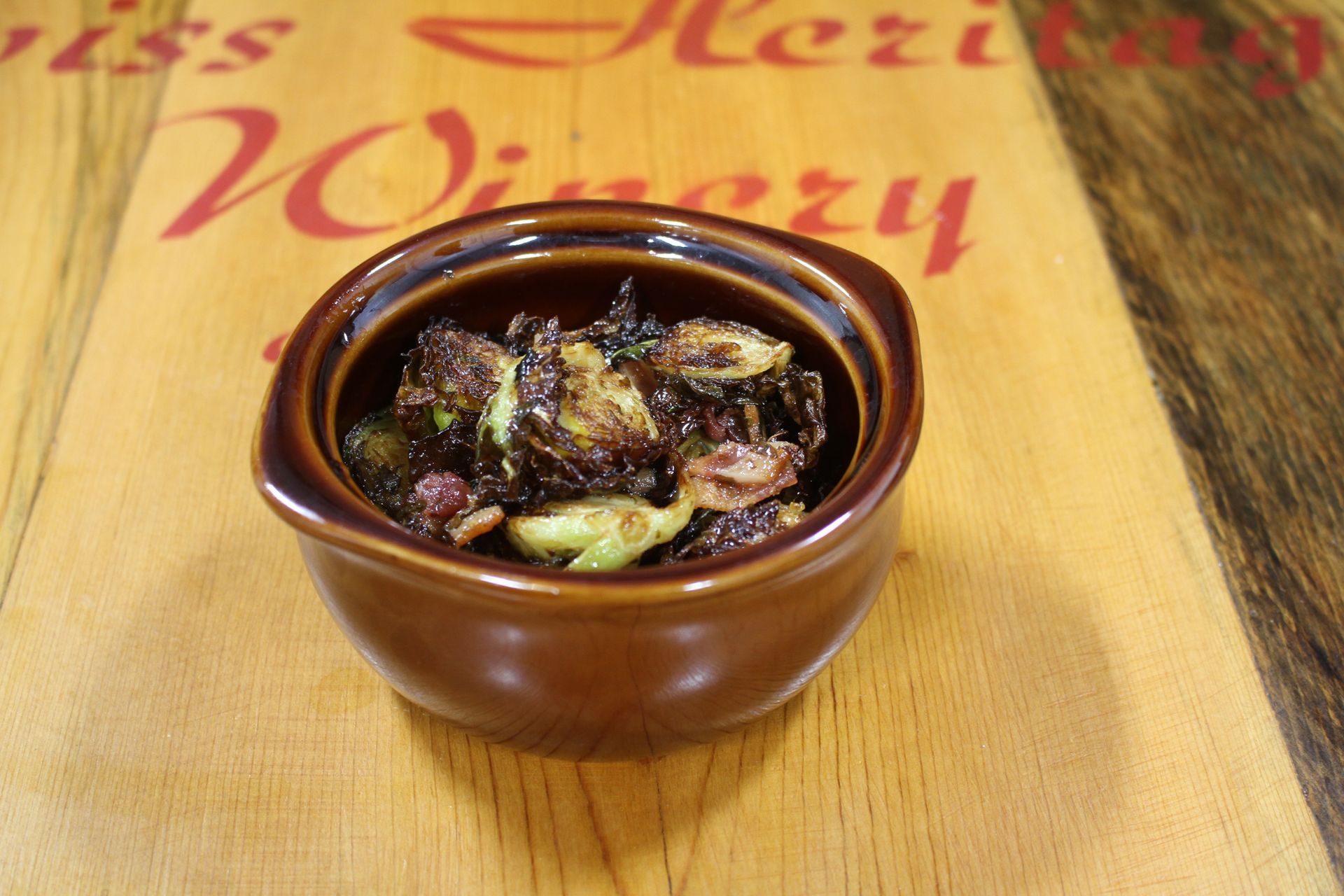 Brown ramekin filled with roasted Brussels sprouts on wooden surface.