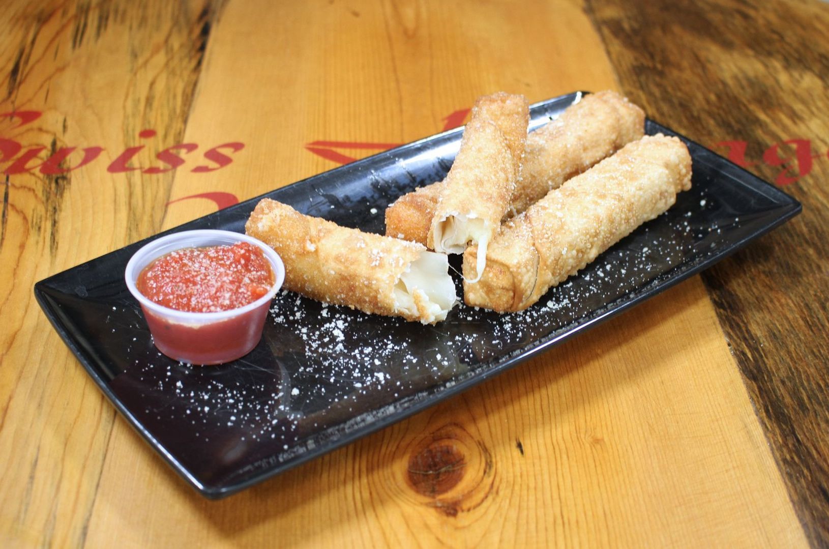 Mozzarella sticks with marinara sauce on a black rectangular plate, wooden table.