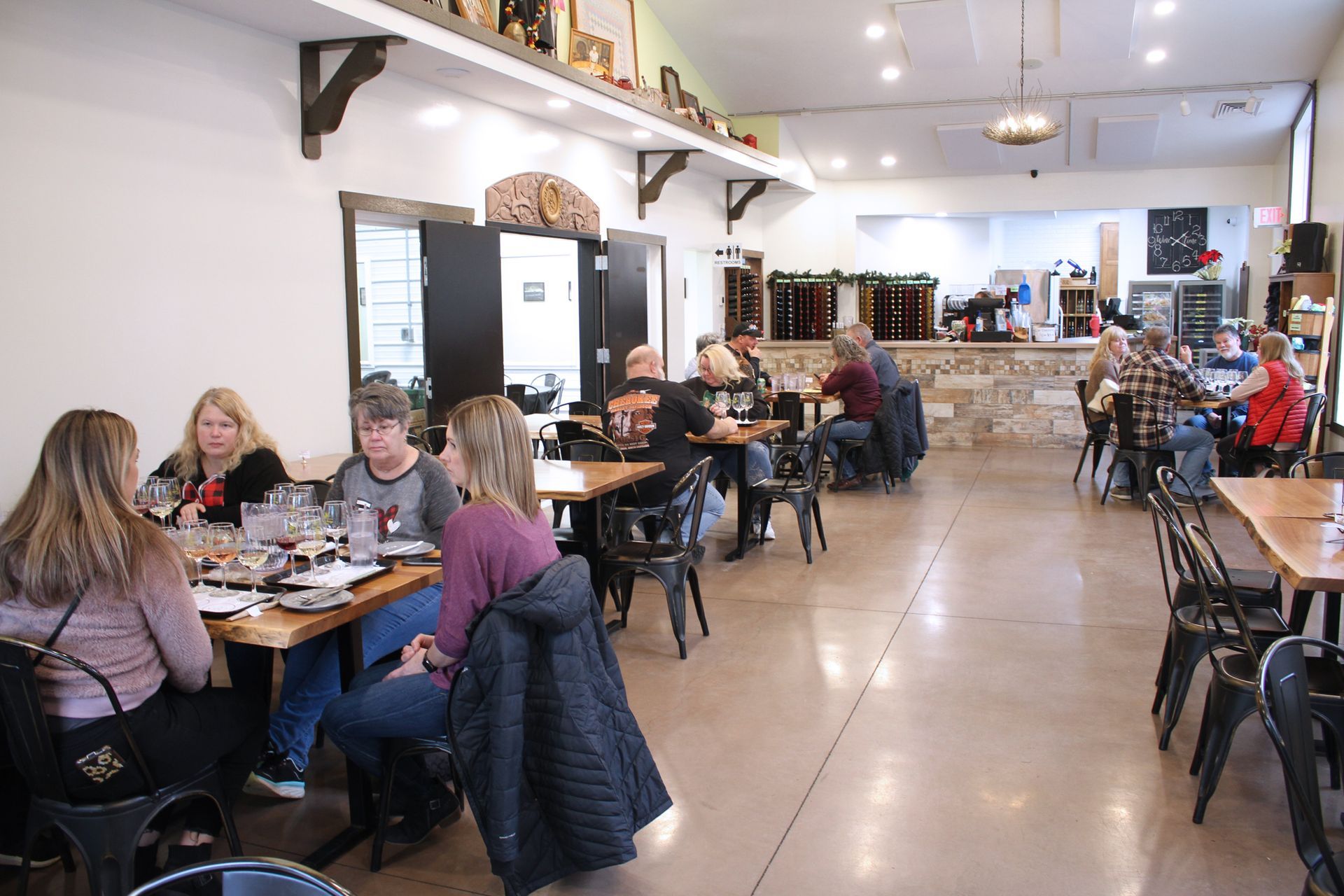 Interior of a restaurant with people seated at tables, eating and conversing. Bright room with a bar area in the background.