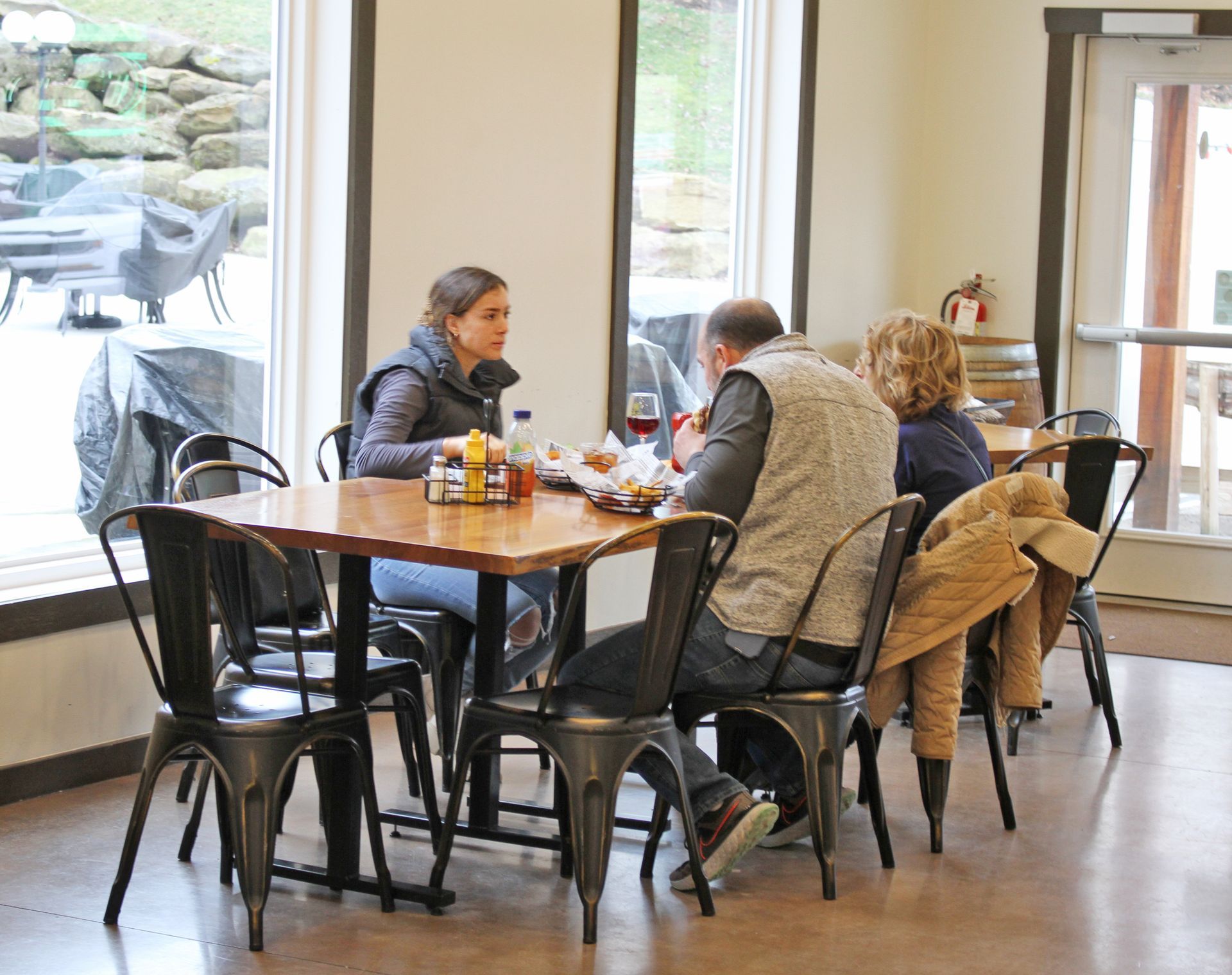 People seated at a table in a restaurant. Sunlight streams in. Plates of food are present.