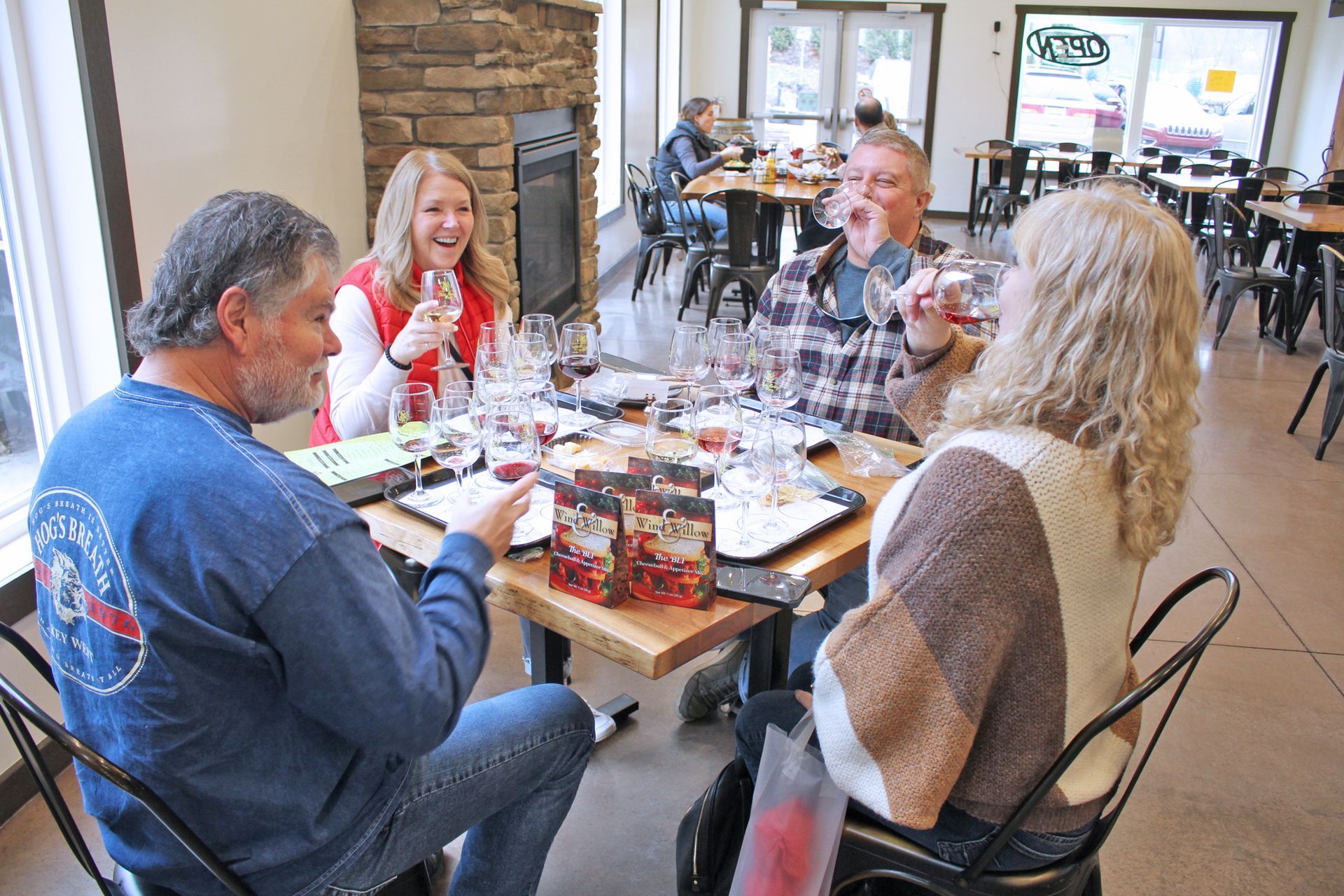 Four people at a table indoors, tasting wine. A fireplace and other diners are visible.