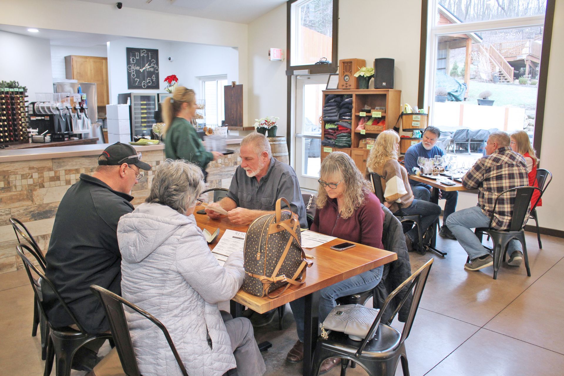 People seated at tables in a tasting room, conversing and sampling drinks. A bar is visible in the background.