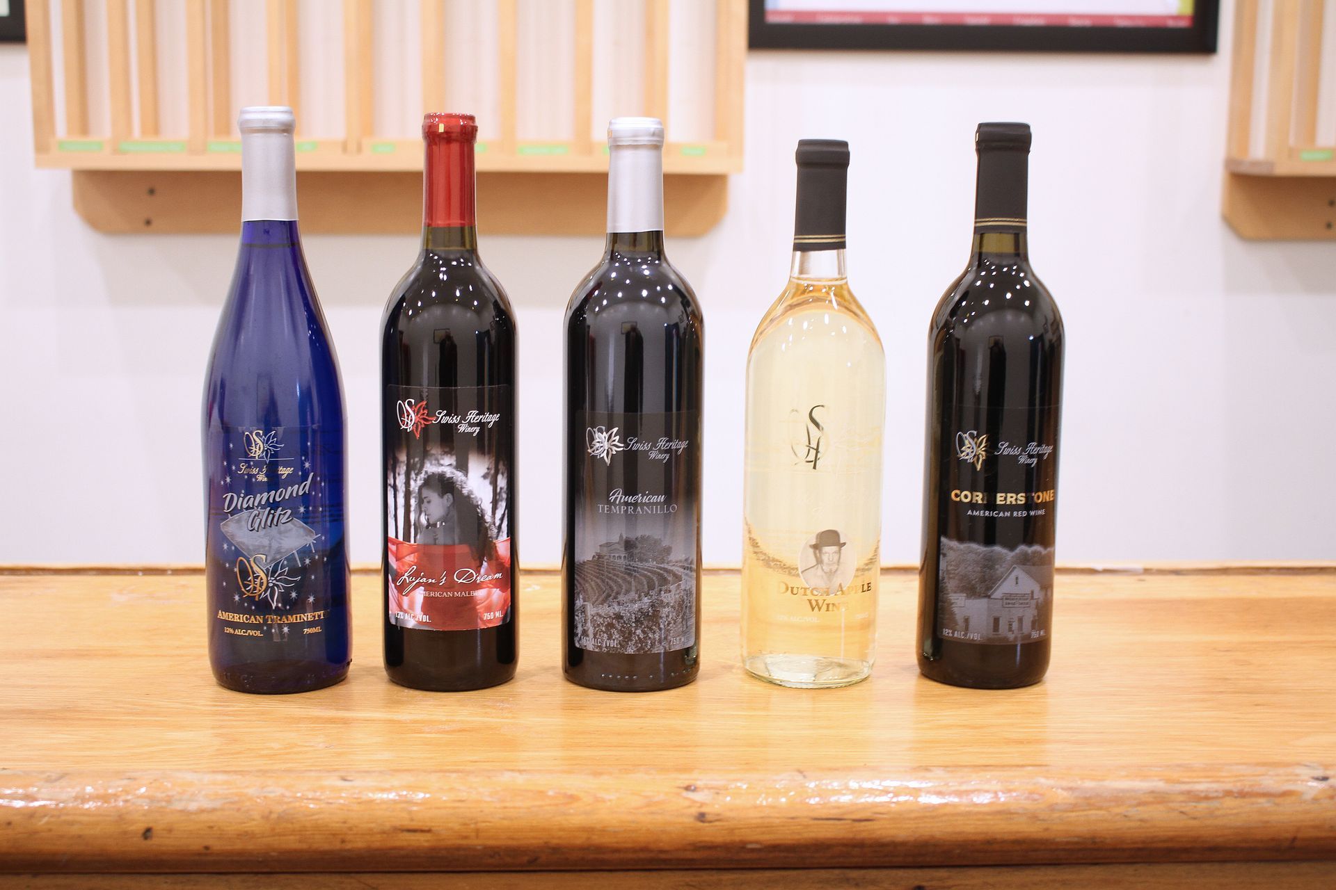 Five wine bottles with colorful labels on a wooden surface.