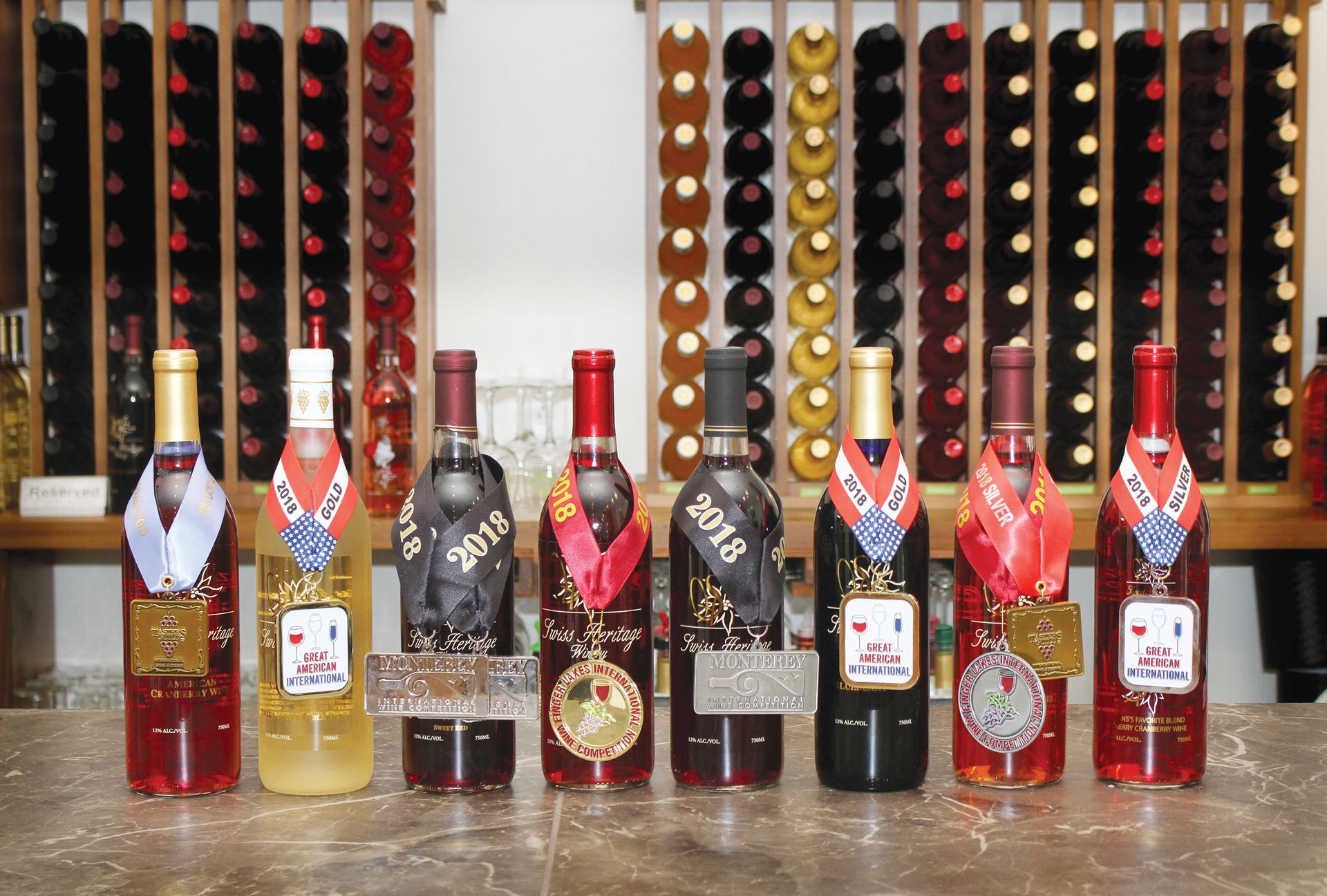 Eight wine bottles with medals on a bar, wine racks in the background.