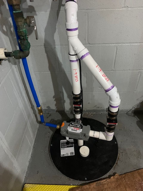 A water-powered backup sump pump system installed on a basement floor, with PVC piping connected to the main water line.