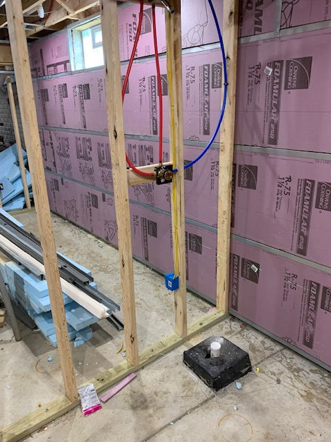 Framed basement walls with pink foam insulation, plumbing pipes, and a shower drain installed on a concrete floor.