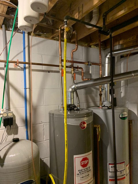 Basement utility area showing two water heaters, copper piping, and a yellow flexible gas line against a block wall.