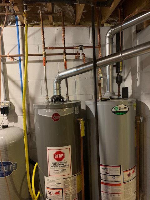 Two residential water heaters connected to copper pipes and silver exhaust venting in a basement utility area.
