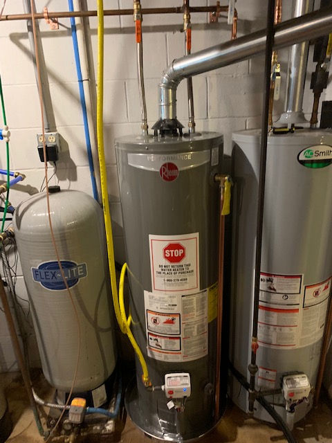 A mechanical room featuring a Flexcon expansion tank beside two Rheem water heaters with metal venting pipes.