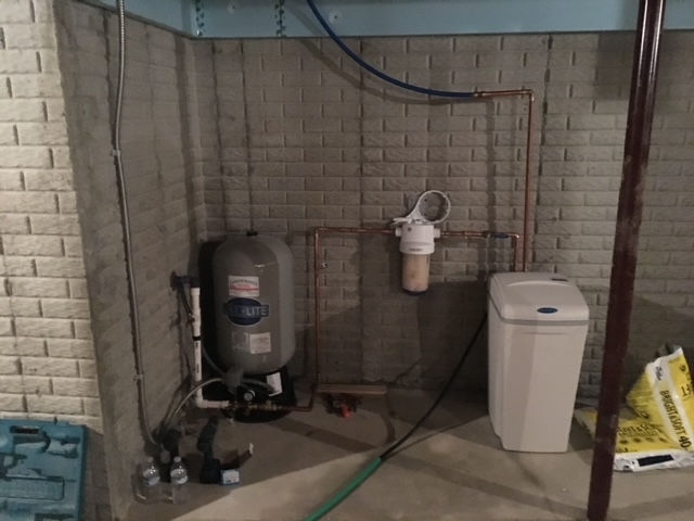 A residential water system featuring a grey pressure tank, a wall-mounted water filter, and a white salt brine tank.