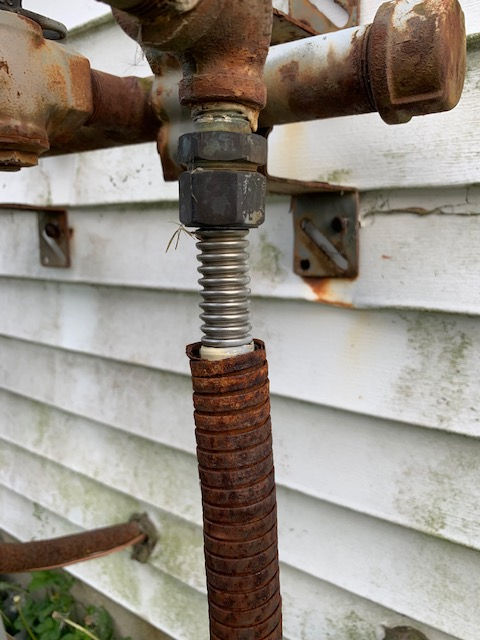 Rusty outdoor plumbing connection with a corrugated metal pipe fitting against white exterior siding.