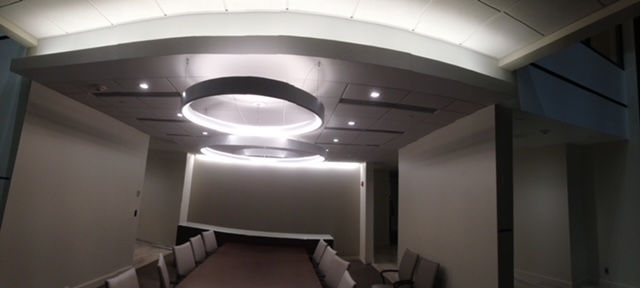 A modern boardroom with a long table, chairs, and circular pendant lights suspended from a tiered, illuminated ceiling.