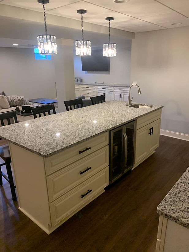 A kitchen island with cream cabinets, speckled granite countertops, and three pendant lights in a basement living space.