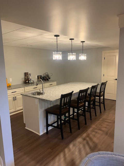 A kitchen island with a granite countertop and four dark wooden bar stools, situated in a basement room with light walls.