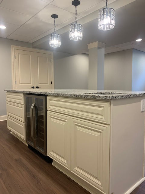 An island with cream-colored cabinets, a built-in wine cooler, and granite countertops under three hanging pendant lights.