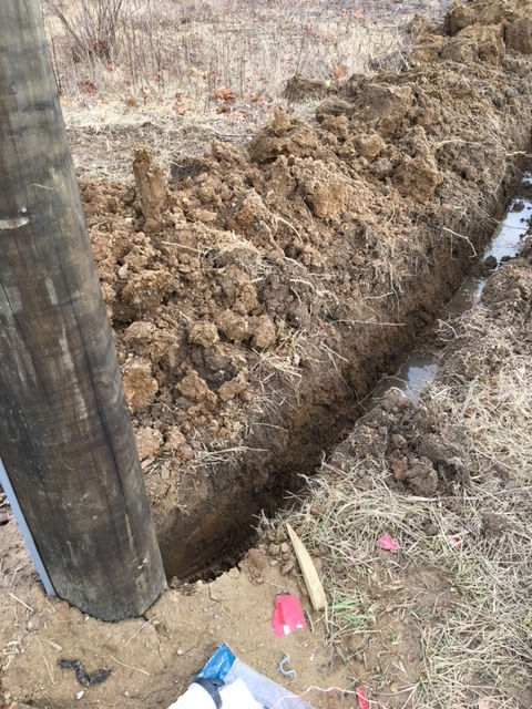 A deep, muddy trench dug into the ground next to a wooden utility pole.