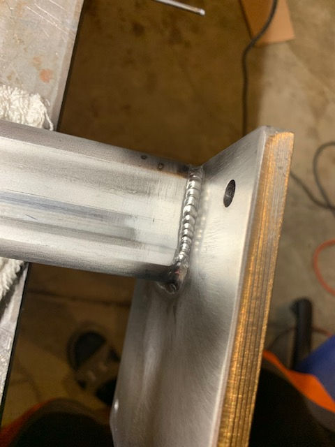 Close-up of a clean metal T-weld joint connecting a square steel tube to a flat mounting plate.