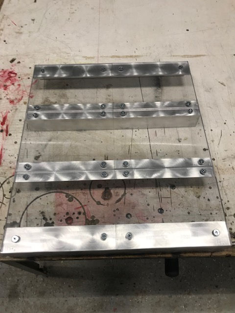 Four parallel metal strips are fastened to a flat, stained workbench surface.