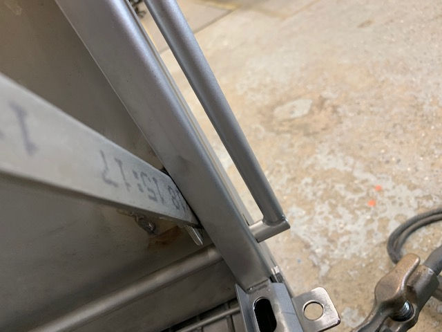 A close-up view of a metal structure with a bracket and a strip of material marked with numbers, against a concrete floor.